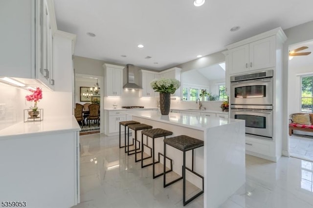 4 Greenbriar Ct, Mount Olive Twp, NJ 07836 - kitchen featuring double oven, wall chimney exhaust hood, a breakfast bar, light marble finish flooring, and a center island