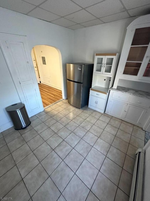 kitchen with freestanding refrigerator, arched walkways, white cabinets, a drop ceiling, and glass insert cabinets