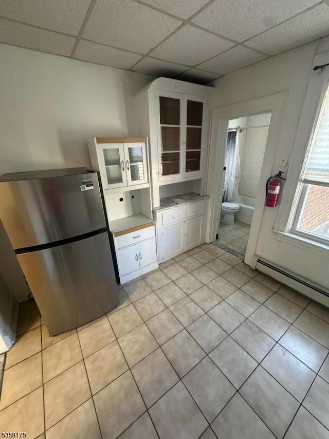 kitchen featuring freestanding refrigerator, a drop ceiling, white cabinets, a baseboard heating unit, and light countertops