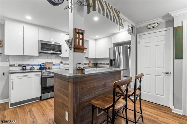 85 Smithfield Ct, Bernards Twp, NJ 07920 - kitchen featuring stainless steel appliances, dark countertops, crown molding, a breakfast bar area, and light wood-type flooring