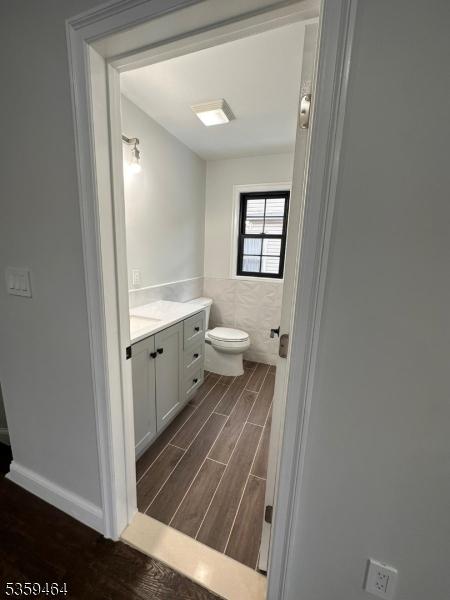 228 78th St, North Bergen Twp, NJ 07047 - half bathroom featuring wood finished floors, vanity, toilet, tile walls, and wainscoting