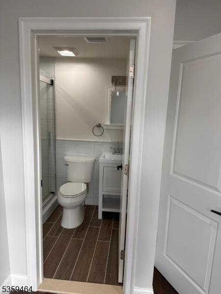 228 78th St, North Bergen Twp, NJ 07047 - bathroom with vanity, toilet, a shower stall, wood finish floors, and tile walls