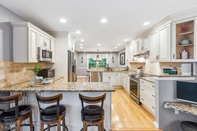 2406 Jamestown Cmn, Hillsborough Twp, NJ 08844 - kitchen with appliances with stainless steel finishes, a peninsula, under cabinet range hood, light stone counters, and recessed lighting