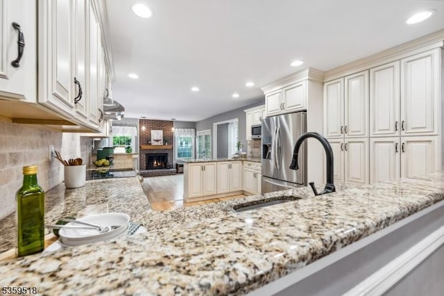 2406 Jamestown Cmn, Hillsborough Twp, NJ 08844 - kitchen with appliances with stainless steel finishes, light stone counters, backsplash, a peninsula, and a fireplace