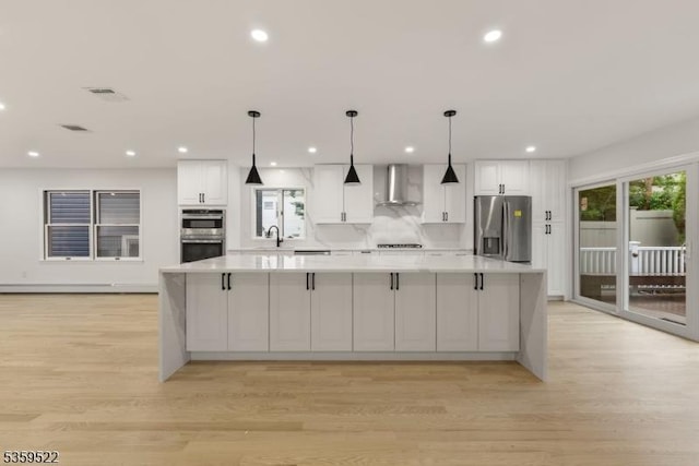 409 Washington St, Carlstadt Boro, NJ 07072 - kitchen featuring appliances with stainless steel finishes, wall chimney range hood, light countertops, white cabinetry, and light wood-style floors