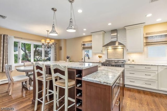 55 Nomahegan Ct, Cranford Twp, NJ 07016 - kitchen with wall chimney exhaust hood, an island with sink, dark wood finished floors, light stone counters, and decorative light fixtures