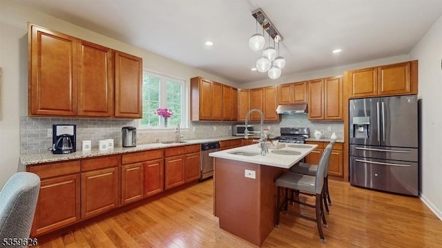 612 Magnolia Rd, North Brunswick Twp, NJ 08902 - kitchen featuring appliances with stainless steel finishes, under cabinet range hood, light wood-style floors, tasteful backsplash, and a kitchen island with sink