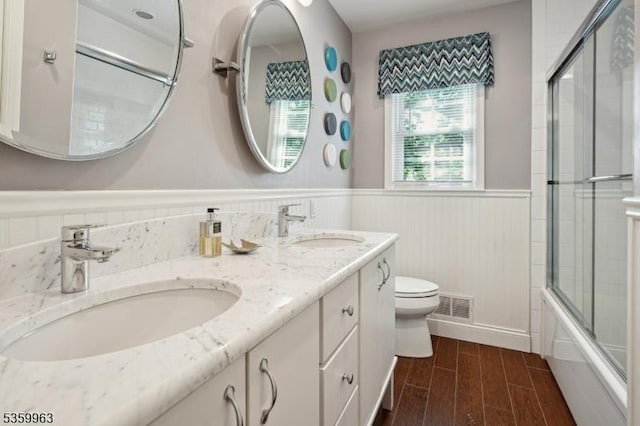 23 Parkview Rd, Chatham Twp, NJ 07928 - bathroom featuring toilet, a wainscoted wall, double vanity, bath / shower combo with glass door, and wood finished floors