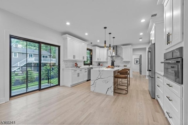 10 Wilson Ave, Wayne Twp, NJ 07470 - kitchen with wall chimney exhaust hood, stainless steel appliances, a kitchen breakfast bar, a center island, and light wood-style flooring