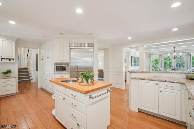5 Barry Ln, Millburn Twp, NJ 07078 - kitchen featuring a sink, a kitchen island with sink, white cabinetry, built in appliances, and a wainscoted wall