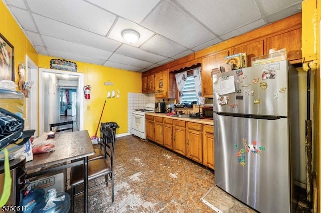 159 2nd St, Elizabeth City, NJ 07206 - kitchen with freestanding refrigerator, white gas range, a drop ceiling, light countertops, and brown cabinets