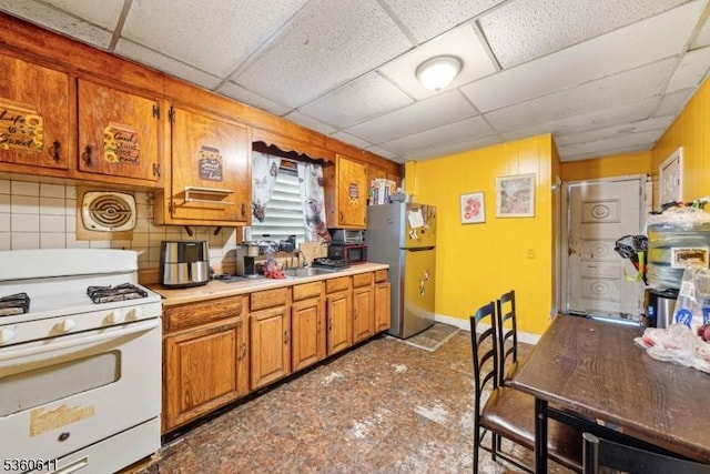 159 2nd St, Elizabeth City, NJ 07206 - kitchen with white gas range, freestanding refrigerator, brown cabinetry, a drop ceiling, and light countertops