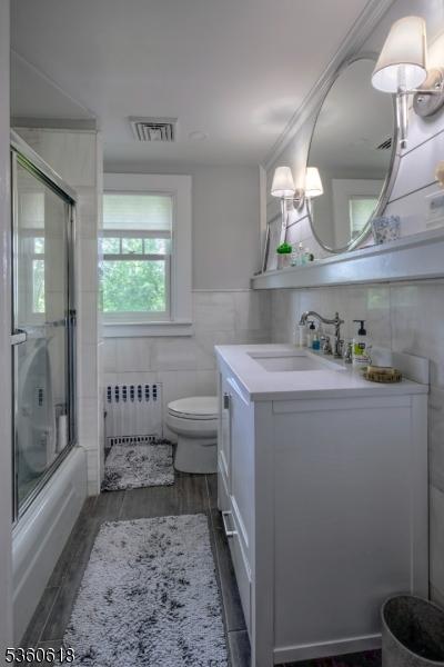 22 Somerset Ave, Bernardsville Boro, NJ 07924 - bathroom with radiator, vanity, tile walls, shower / bath combination with glass door, and wood finished floors