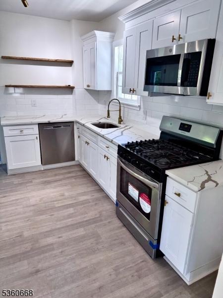 67 Mead St, Newark City, NJ 07106 - kitchen with appliances with stainless steel finishes, open shelves, a sink, white cabinetry, and tasteful backsplash