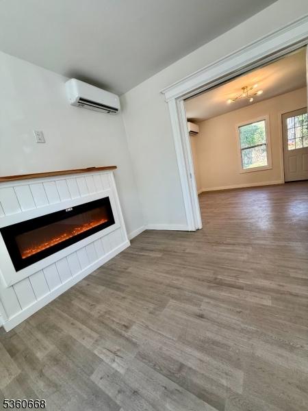 67 Mead St, Newark City, NJ 07106 - unfurnished living room featuring a wall mounted AC, a glass covered fireplace, wood finished floors, and baseboards