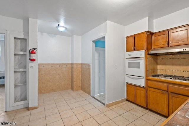 30-32 Geneva St, Elizabeth City, NJ 07206 - kitchen with white appliances, a warming drawer, under cabinet range hood, brown cabinetry, and light tile patterned floors
