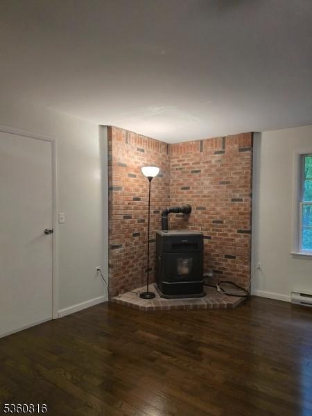 103 Mountain Top Rd, Lebanon Twp, NJ 08826 - unfurnished living room with a wood stove, wood finished floors, baseboards, and brick wall