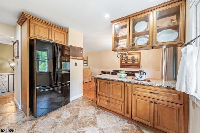 39 Fox Chase Run, Hillsborough Twp, NJ 08844 - kitchen with freestanding refrigerator, light stone counters, brown cabinets, glass insert cabinets, and a wainscoted wall