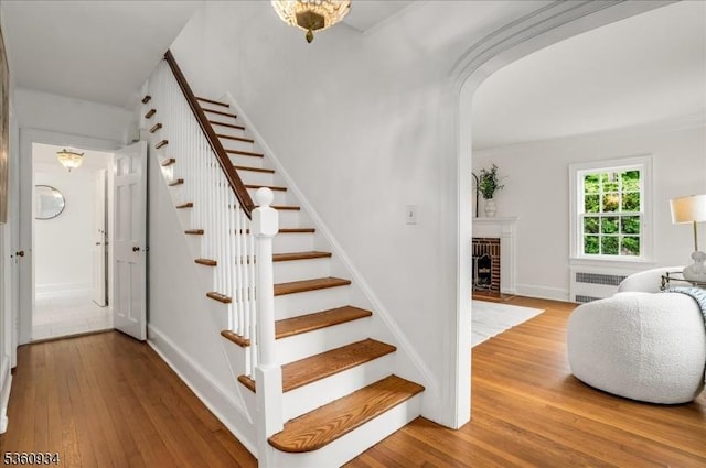 168 Grove St, Montclair Twp, NJ 07042 - staircase with radiator heating unit, hardwood / wood-style floors, a fireplace, arched walkways, and baseboards
