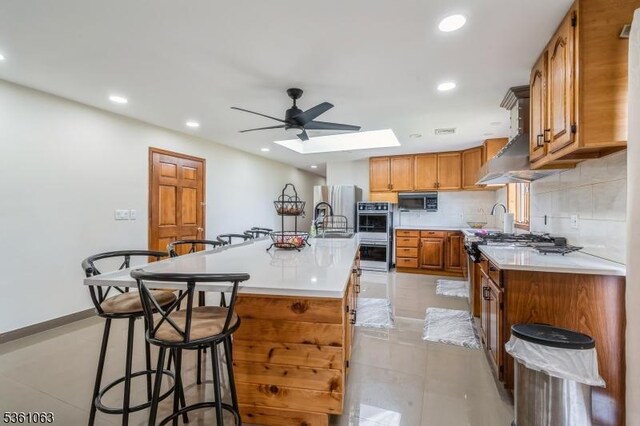 30 Claridge Ln, Raritan Twp, NJ 08822 - kitchen featuring brown cabinets, a center island with sink, ceiling fan, a skylight, and a kitchen breakfast bar