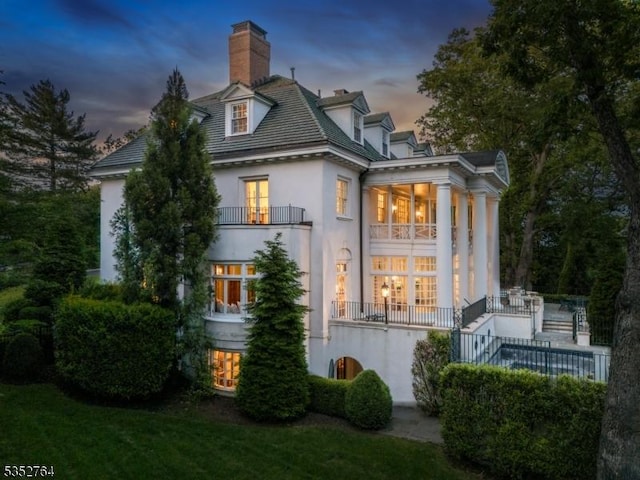 10 Rowan Rd, Summit City, NJ 07901 - back of property at dusk with stucco siding, a balcony, and a chimney