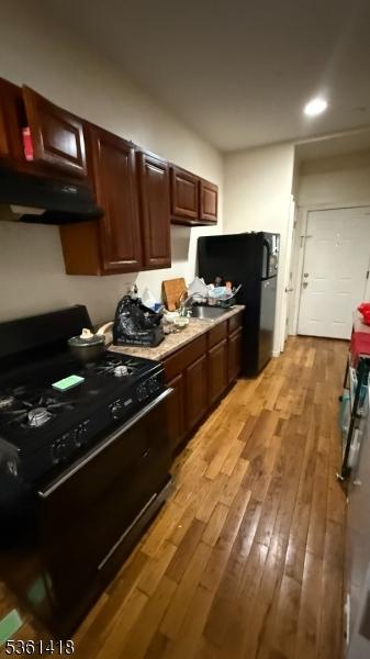 28 1st St, Elizabeth City, NJ 07206 - kitchen featuring black appliances, under cabinet range hood, light wood finished floors, dark brown cabinets, and light countertops