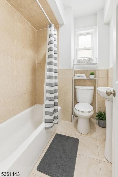 276 5th Ave, Paterson City, NJ 07524 - bathroom featuring tile patterned floors, tile walls, toilet, shower / tub combo with curtain, and a wainscoted wall