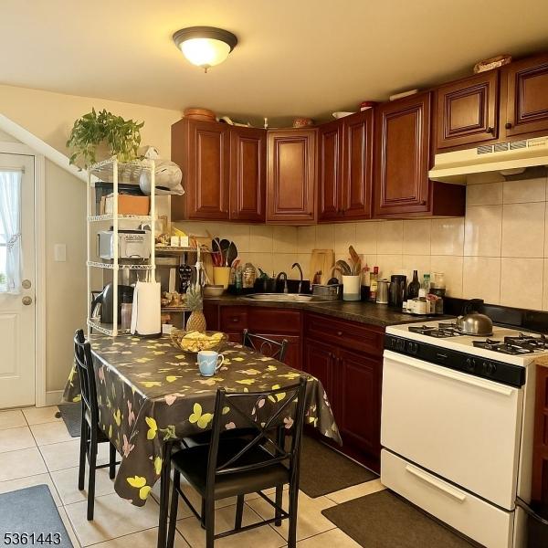 276 5th Ave, Paterson City, NJ 07524 - kitchen with white range with gas cooktop, under cabinet range hood, a sink, light tile patterned flooring, and decorative backsplash
