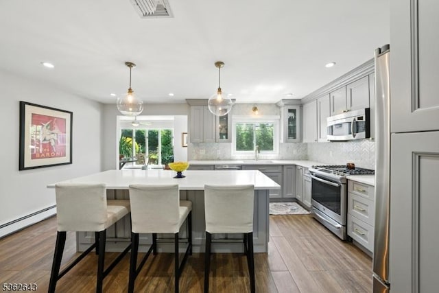 80 Rose St, Wood-Ridge Boro, NJ 07075 - kitchen featuring stainless steel appliances, gray cabinetry, light countertops, dark wood-style floors, and a breakfast bar