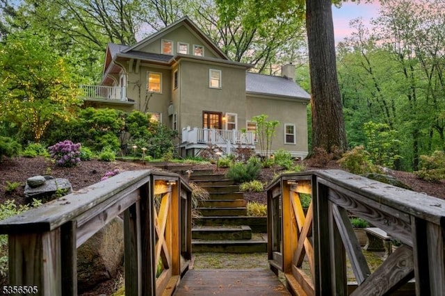 34 Crane Rd, Mountain Lakes Boro, NJ 07046 - back of house at dusk featuring stairway, a wooden deck, stucco siding, and a chimney
