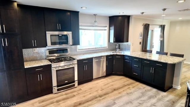 151 2nd St, Franklin Twp, NJ 08873 - kitchen featuring appliances with stainless steel finishes, a peninsula, decorative backsplash, light stone counters, and light wood-style flooring