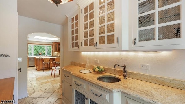 80 Clark Rd, Bernardsville Boro, NJ 07924 - kitchen with glass insert cabinets, stainless steel dishwasher, arched walkways, light stone countertops, and light stone finish floors