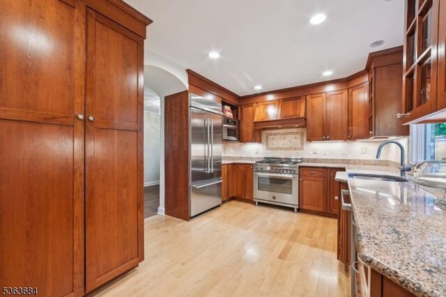 135 Weston Ave, Chatham Boro, NJ 07928 - kitchen featuring high quality appliances, light wood-style floors, brown cabinetry, light stone countertops, and arched walkways