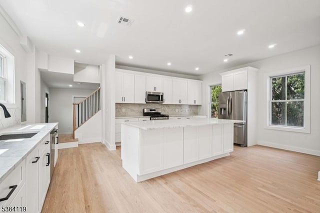 24 Tuers Pl, Montclair Twp, NJ 07043 - kitchen with stainless steel appliances, light wood-type flooring, backsplash, white cabinetry, and a kitchen island