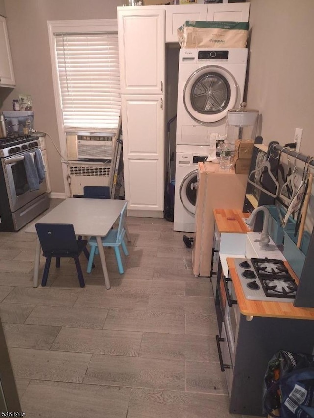 341 N Grove St, East Orange City, NJ 07017 - kitchen with stainless steel range with gas stovetop, stacked washer / dryer, white cabinetry, cooling unit, and light wood-style flooring