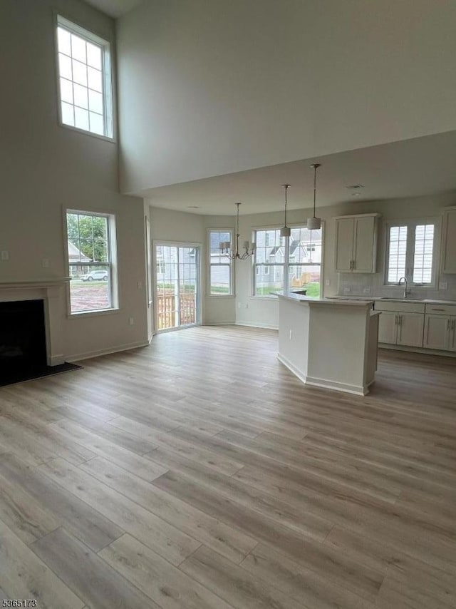 77 Norton Rd, Hillsborough Twp, NJ 08844 - unfurnished living room with a chandelier, light wood finished floors, a towering ceiling, and a fireplace