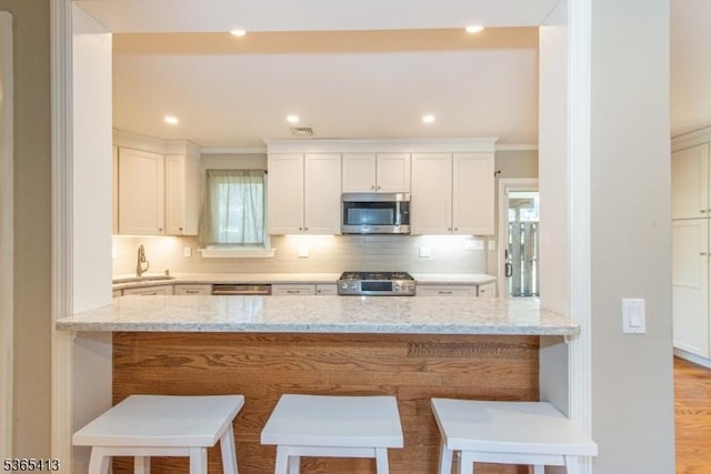 9 Hilary Ct, Vernon Twp, NJ 07460 - kitchen with appliances with stainless steel finishes, light stone counters, a kitchen bar, ornamental molding, and recessed lighting