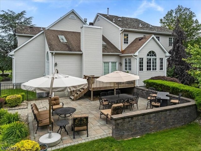 33 Gates Pl, Wayne Twp, NJ 07470 - back of house with a patio, outdoor dining area, a shingled roof, a chimney, and a wooden deck