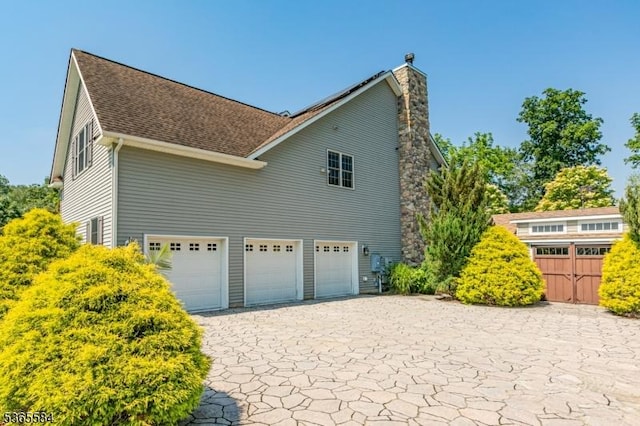 4 Wingover Farm Ct, Raritan Twp, NJ 08822 - view of side of home featuring a garage, a chimney, roof with shingles, and decorative driveway