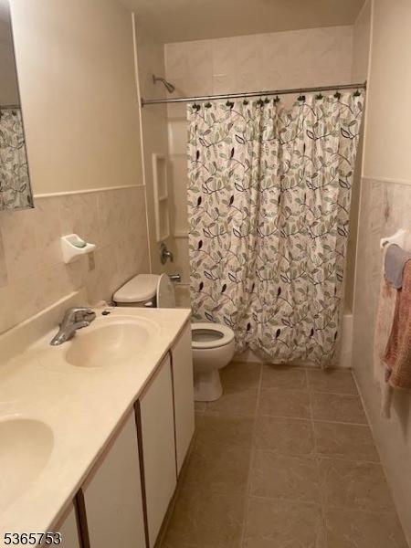 550-552 S 19th St, Newark City, NJ 07103 - bathroom featuring tile walls, tile patterned flooring, shower / bathtub combination with curtain, double vanity, and wainscoting