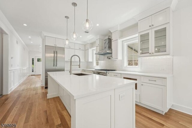 151 Center Ave, Chatham Boro, NJ 07928 - kitchen with wall chimney exhaust hood, built in fridge, white cabinets, backsplash, and a center island with sink