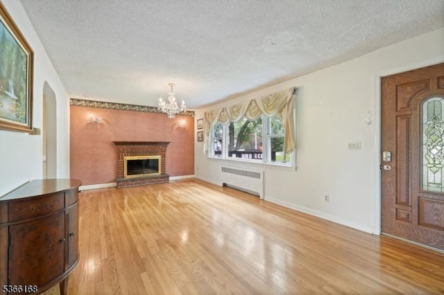 3 Casey Ave, East Hanover Twp, NJ 07936 - unfurnished living room featuring radiator heating unit, a textured ceiling, light wood-style floors, a chandelier, and a brick fireplace