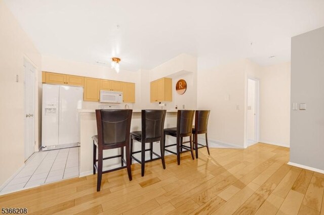 2112 Schindler Ln, Wayne Twp, NJ 07470 - kitchen with white appliances, light wood-style floors, a peninsula, light countertops, and a breakfast bar