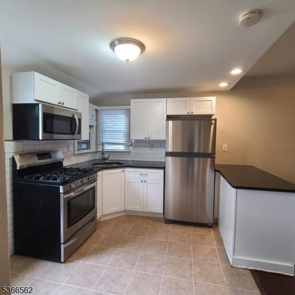 16 Ransome Pl, Plainfield City, NJ 07063 - kitchen with stainless steel appliances, backsplash, white cabinetry, dark countertops, and light tile patterned floors
