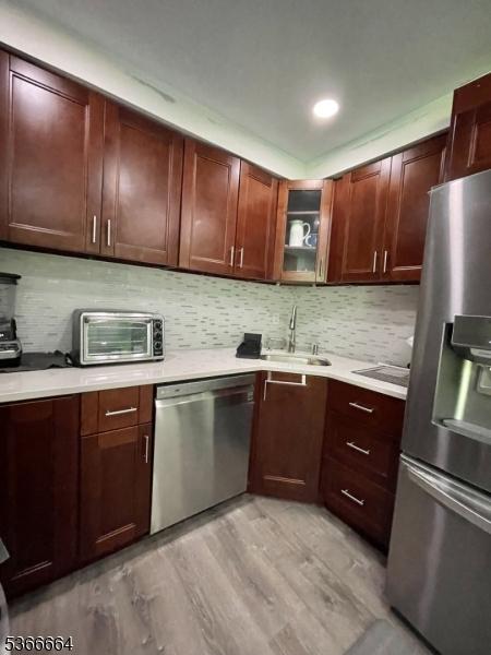 23D Hanover Sq Unit 23, Middlesex Boro, NJ 08846 - kitchen with appliances with stainless steel finishes, light wood finished floors, light countertops, decorative backsplash, and glass insert cabinets