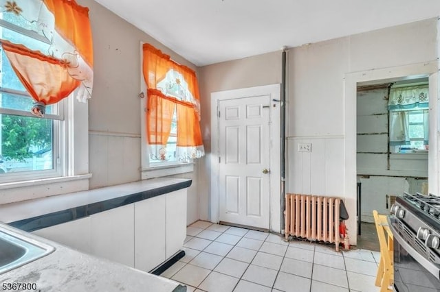 1705 Essex St, Rahway City, NJ 07065 - kitchen featuring radiator heating unit, stainless steel gas range, light tile patterned floors, white cabinetry, and a wainscoted wall