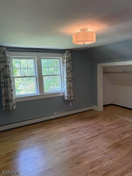 196 Littleton Rd, Morris Plains Boro, NJ 07950 - unfurnished bedroom featuring wood finished floors, multiple windows, a baseboard heating unit, and a closet