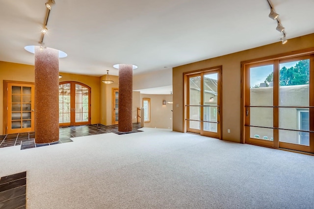 unfurnished living room featuring track lighting, dark colored carpet, and french doors