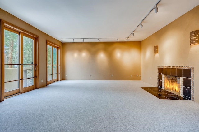 carpeted spare room featuring track lighting and a tile fireplace