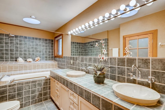 bathroom with tasteful backsplash, a relaxing tiled bath, toilet, dual bowl vanity, and tile floors